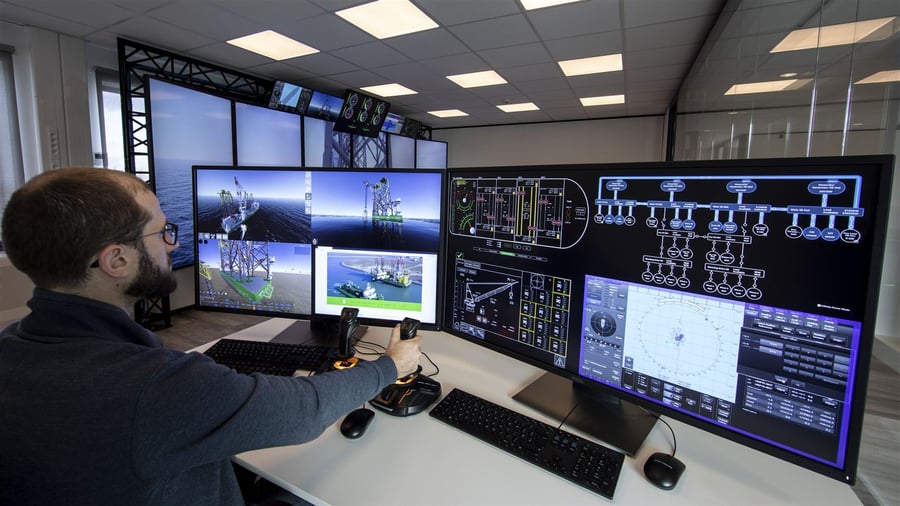 Operator at a desk with large screens and a screen wall behind Operator at a desk with large screens and a screen wall behind