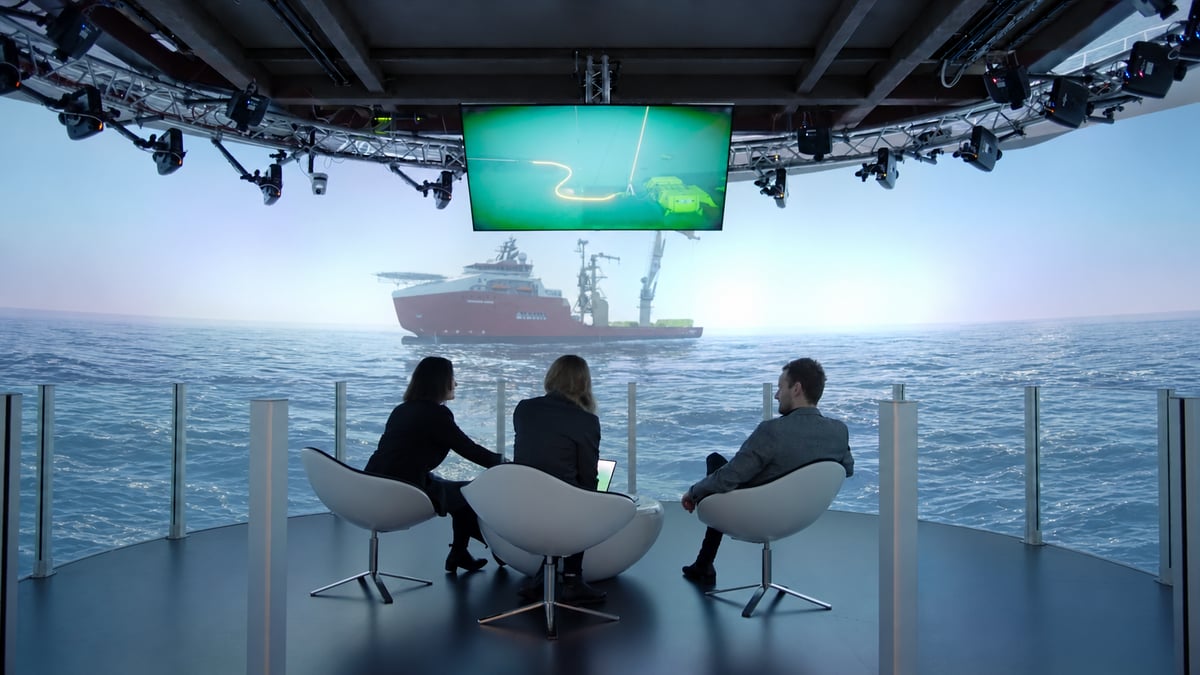 Three people discussing an operation in front of a simulated vessel at sea Three people discussing an operation in front of a simulated vessel at sea