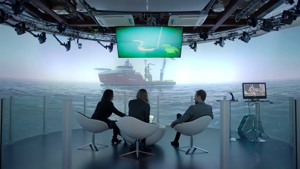Three people discussing an operation in front of a simulated vessel at sea Three people discussing an operation in front of a simulated vessel at sea